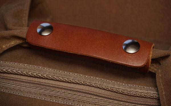 A brown fabric bag featuring a leather handle with silver studs
