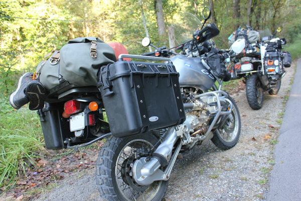 Two adventure motorcycles parked by a wooded path