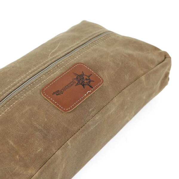 A brown waxed canvas pouch with a leather label and zipper
